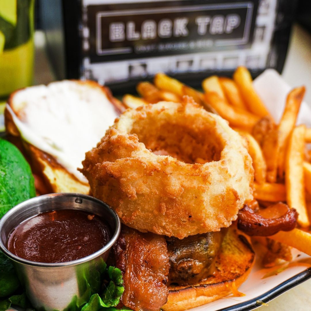 Loaded Black Tap burger topped with crispy onion rings and served with fries